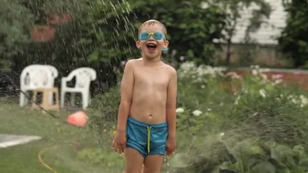 Смешной мальчик в защитных очках, кричащий, веселящийся под падающими брызгами воды — стоковое видео