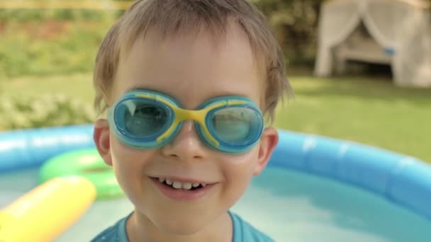 Detailní tvář legrační chlapeček brýle pózování na dvorku s nafukovací gumový bazén — Stock video