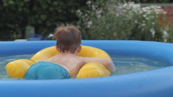 Veselé mužské dítě plovoucí na žluté záchranné bóji v nafukovacím gumovém dětském bazénu — Stock video