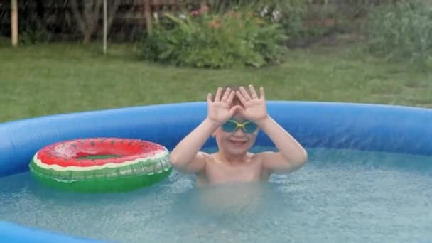 Aktivní malý chlapec plovoucí na venkovní nafukovací gumový bazén skrývající se před pádem stříkance — Stock video