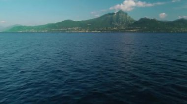 Parlak deniz manzarası boyunca ilerleyen inanılmaz bir görüntü. Etrafı yüksek ve güzel dağlarla çevrili berrak suyun üzerinde uçan temiz doğal deniz manzarası ve gün ışığında ufuk çizgisi.