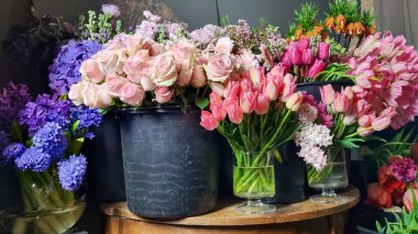 Çiçekçinin içinde siyah kovalarda sergilenen renkli taze çiçek çeşitleri. Laleler, güller, çiçek pazarında ahşap bir masa etrafında düzenlenmiş karışık bahar çiçekleri gibi çeşitli çiçekler. 