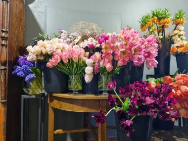 Çiçekçinin içinde siyah kovalarda sergilenen renkli taze çiçek çeşitleri. Laleler, güller, çiçek pazarında ahşap bir masa etrafında düzenlenmiş karışık bahar çiçekleri gibi çeşitli çiçekler. 