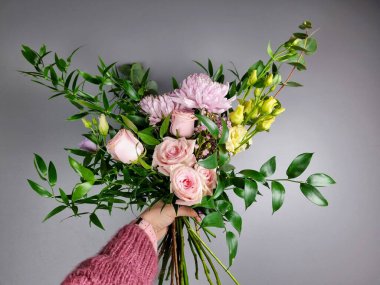 Yumuşak pembe güllerden, kasımpatılardan ve tarafsız gri bir arkaplanda serpilmiş taze yeşillikten yapılmış narin bir çiçek buketi. Çiçekçide çiçekçi