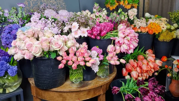Çiçekçinin içinde siyah kovalarda sergilenen renkli taze çiçek çeşitleri. Laleler, güller, çiçek pazarında ahşap bir masa etrafında düzenlenmiş karışık bahar çiçekleri gibi çeşitli çiçekler. 