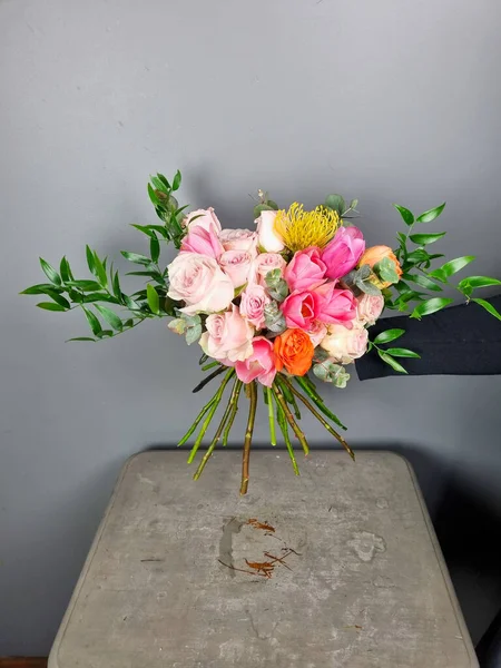 Renkli çiçek buketi pembe güller ve yemyeşil çiçeklerle düzenlenmiş, tarafsız gri arka planda sergileniyor. Çiçekçide çiçekçi
