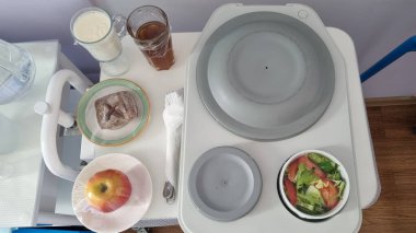 Hastane yemek tepsisinin en üst görüntüsü. Komodinin üzerinde yiyecek ve içecekler var. Tabaklar, salata, meyve ve içeceklerle tıbbi beslenme konsepti, temiz minimum bileşim.