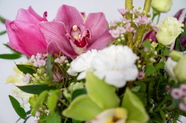 Orkide çiçekleri ve karışık yeşilliklerin yer aldığı renkli bir çiçek düzeninin yakın çekimi. Pembe, yeşil ve beyaz tonlu dekoratif buket.