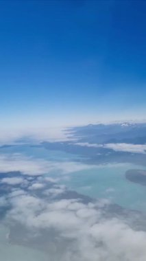 Kıyı şeridinin havadan görünüşü, bulutların üstündeki uçaktan görünen göller ve dağlar. Uçuş, seyahat ve turizm konsepti sırasında mavi gökyüzü ve su manzarası.