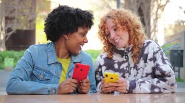 İki neşeli genç kadın hevesle akıllı telefonlarını kullanıyor, mobil uygulamalarla uğraşırken keyifli bir deneyim paylaşıyorlar, teknolojiye ve birbirleriyle bağlantıya dalmışlar..