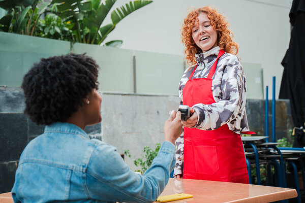 A woman cheerfully engaging in a payment transaction, handing over a credit card with a smile, showcasing a friendly interaction that captures the essence of customer service and positivity.