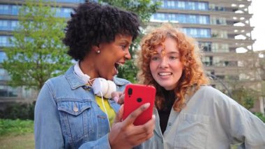İki hevesli kadın, akıllı telefonlarında heyecan verici bir uygulamayı keşfederken keyifli bir anın tadını çıkarıyorlar. Eğlenceli bir deneyim için birbirleriyle gülüşmeler ve gülümsemeler paylaşıyorlar..