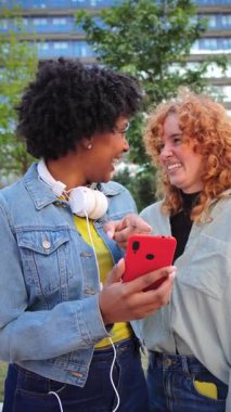 Neşeli genç kadınlar heyecanlı bir şekilde cep telefonlarıyla meşgul, birlikte gülüşmeler ve keyifli bir an paylaşıyorlar, canlı bir atmosferde teknolojiyle arkadaşlığın ve bağlantının sevincini gösteriyorlar..