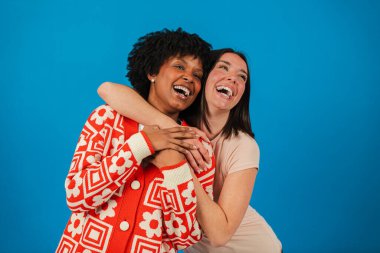 İki neşeli kadın neşeyle kucaklaşıp gülüyorlar. Güçlü dostluklarını ve mutluluklarını yansıtan hoş bir anı paylaşıyorlar. Kahkahalarla ve gerçek bir sevgiyle.