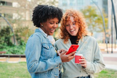 İki neşeli arkadaş, çeşitli mobil uygulamaları keşfetmek ve neşeli bir atmosferde kahkaha ve iletişimi paylaşmak için bir akıllı telefonla hoş bir şekilde meşgul oluyorlar..