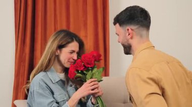 Neşeli bir kadın, aşkı sembolize eden sevgi dolu eşinden çarpıcı bir buket kırmızı gül kabul eder. Sıcak renkler, duygusal bağlantılarını göstererek mahrem anı güçlendirir..