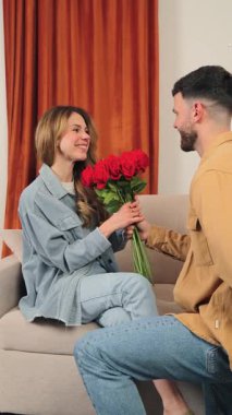 Zevkli bir kadın, partnerinden çarpıcı bir buket kırmızı gül alırken gülümser. Sıcak, kapalı bir mekanda sevgi ve şefkat dolu bir an gösterir. Romantik durumlar için mükemmel bir an..