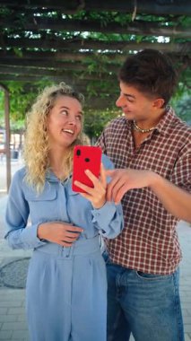 Neşeli bir çift, gülüşlerini ve mutluluklarını gösteren akıllı bir telefonla hoş bir selfie çeker. Sevgi ve bağlarla dolu, neşeli bir anda eğleniyorlar.