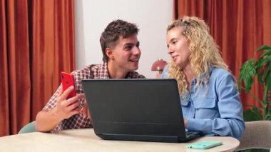 Mutlu çift, eğlenceli çevrimiçi etkileşimler ve aktiviteler için dizüstü bilgisayar ve telefon kullanırken kahkaha ve heyecanı paylaşıyor, samimi ve davetkar bir ortamda unutulmaz anlar yaratıyor..