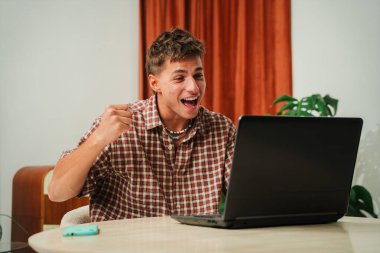 Önemli bir başarı sırasında dizüstü bilgisayarla iletişim kurarken heyecan ve mutluluk ifade eden mutlu bir adam. Neşeli sürprizi kutlamanın ve kazanmanın özünü yakalıyor..