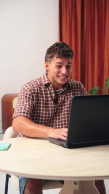 Neşeli genç bir adam dizüstü bilgisayarıyla uğraşırken, bu canlı başarı anında zafer ve mutluluğun heyecanlı bir ifadesini sergiliyor..