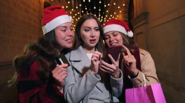 Üç neşeli kadın, neşeli bir atmosferde birlikte kutlama yaparken ve birlikte eğlenirken akıllı bir telefonla gülüşmeler ve heyecan paylaşıyorlar..