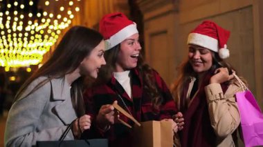 Bayram mevsimini heyecanla kutlayan üç neşeli kadın hediyelerini verirken ve neşeli alışveriş deneyimleri sırasında neşe ve mutluluk dolu kahkahalarla kahkahalarını paylaşırken..