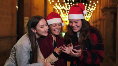 Üç neşeli kadın bayram sezonunu birlikte kutluyor, Noel şenliklerinde telefonlarıyla eğlenirken kahkaha ve eğlencelerini paylaşıyorlar, birbirlerine mutluluk ve sıcaklık saçıyorlar..