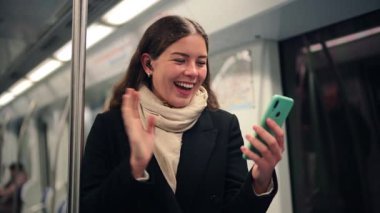 Neşeli genç bir kadın, metroya binerken akıllı telefonuyla sohbete dalmaktan mutlu olur. Gezici dost bir dünyada eğlencesini ve iletişiminin kolaylığını gösterir..