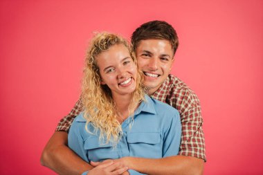 Gülümseyerek doğrudan kameraya bakarken birbirlerini kucaklayan neşeli bir çift. Neşeli ifadeleri, neşeli ve parlak bir atmosferde sevgi ve sıcaklık yayar..