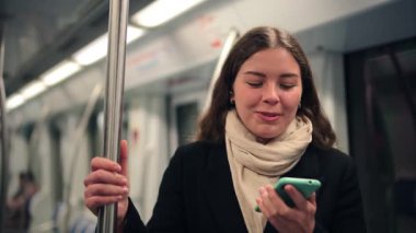 Neşeli genç bir kadın, akıllı telefonunu toplu taşımacılık üzerinden bir çağrı yapmak için kullanırken gülüyor, bir neşe ve etkileşim anında mutluluk ve bağlantı hissini iletiyor..