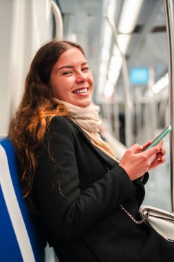 Neşeli bir bayan yolcu metroda otururken akıllı telefonunu mutlulukla kullanıyor, işe ya da okula gidip gelirken cep telefonundaki son uygulamaları incelemeye dalmış.
