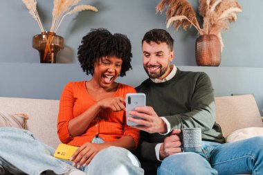 Bir çift, birlikte uygulamaları keşfetmek için akıllı telefon kullanırken heyecanlı bir an yaşıyor. Onların ifadeleri eğlenirken mutluluk ve bağlantıyı yansıtır..