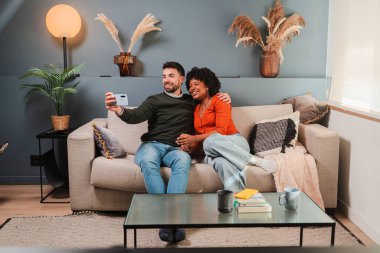 Mutlu çift, akıllı bir telefonla selfie çekerken keyifli bir anı paylaşıyor. Neşeli yüz ifadelerini ve ev ortamlarındaki bağlantılarını yakalıyorlar..