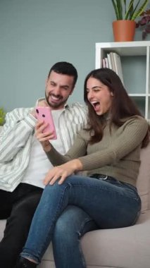 Mutlu çift, bir galibiyeti kutlarken, akıllı telefonlarıyla bağlantının ve heyecan verici ev ortamlarının tadını çıkarıyorlar..