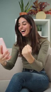 Heyecan ve zafer ifade eden neşeli bir kadın önemli bir başarıyı kutlamak için akıllı telefonunu kullanıyor. Animasyon jestleri, mobil cihazıyla mutluluğu ve bağlılığı yansıtıyor..