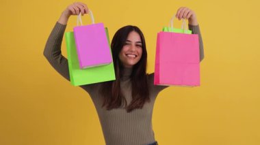 Neşeli kız renkli alışveriş çantalarını gösterirken neşeli bir anda kameraya geniş bir gülümsemeyle, alışveriş deneyimi sırasında mutluluk ve heyecan saçıyor..