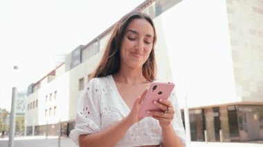 Neşeli kadın akıllı telefonuyla mutlu bir şekilde iletişim kuruyor. Teknolojiye ve bağlantıya dalmış, dışarıdaki fırsatlarla dolu keyifli bir günde..