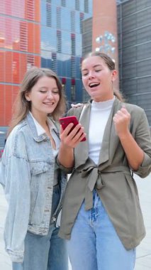 İki hevesli arkadaş mutlu bir anı sevinçle kutlarken aynı anda akıllı bir telefonla iletişim kuruyor ve heyecan verici haberleri paylaşıyorlar. İfadeleri, bu hayat dolu yerde mutluluk ve dostluğu ifade ediyor.