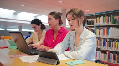 Akademik bir ortamda etkin araştırma ve öğrenim için dizüstü bilgisayar ve tabletlerden yararlanan, takım çalışması ve görevlerine yoğunlaşan üç kendini işine adamış öğrenci