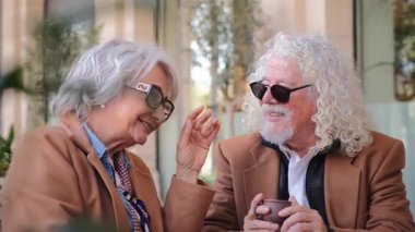 Birbirine eşlik eden yaşlı bir çift, kahve içerken kahkahalarını ve neşeli ifadelerini ve gerçek mutluluklarını paylaşırlar..