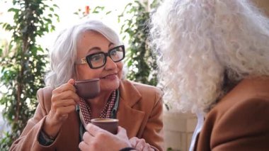 İki yaşlı arkadaş kahveyi yudumlarken, neşeli bir anı paylaşıyorlar, animasyon sohbetleri ve kahkahalarla meşgul oluyorlar, keyifli bir bağ kuruyorlar ve arkadaşlığın sıcaklığını gösteriyorlar..