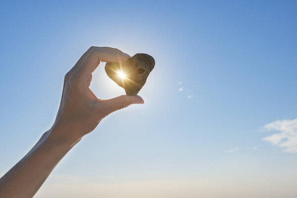 Морской камень в форме сердца в руке женщины, на фоне неба