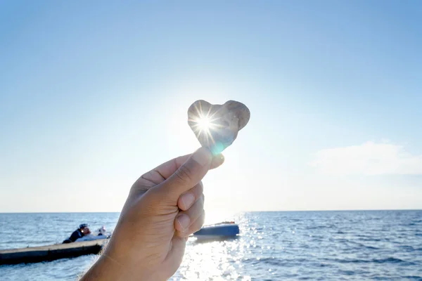 Sea stone in the shape of a heart in a man\'s hand, against the background of the sky and the sea coast
