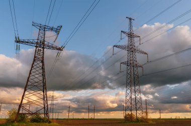 Güzel bulutlu bir gökyüzünün arka planında tarladan geçen yüksek voltajlı elektrik hatları..