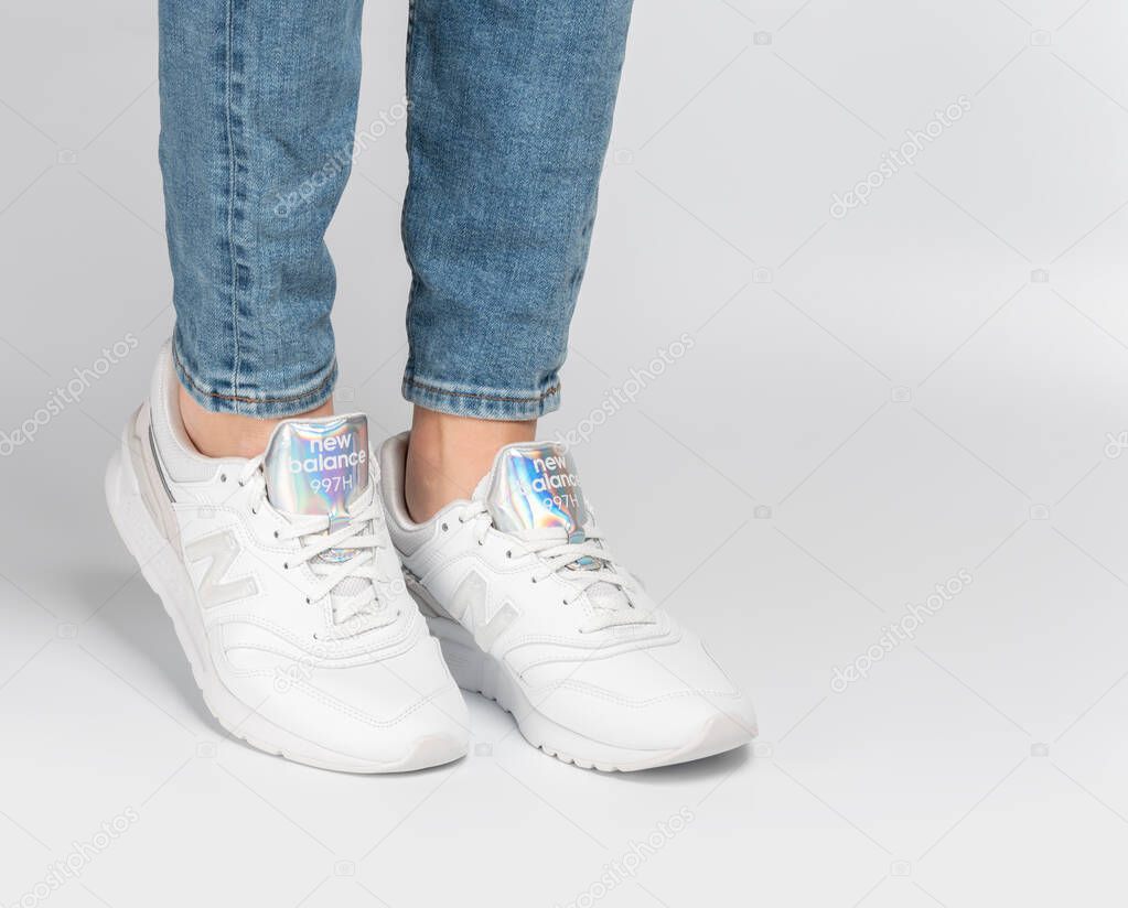 Kiev, Ukraine - January 03, 2021: White women's casual sneakers from New Balance brand on a light background. Young girl in jeans and sneakers on a gray background.