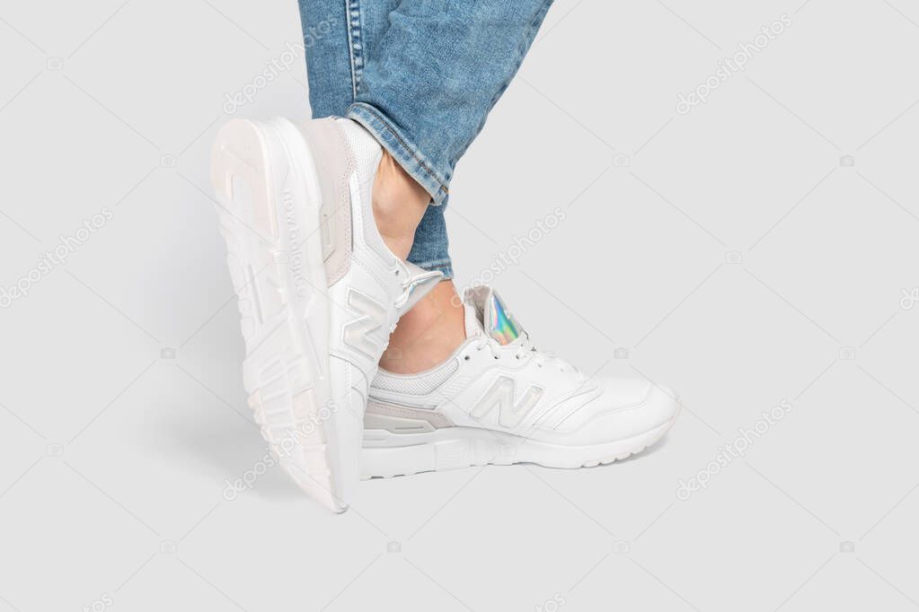 Kiev, Ukraine - January 03, 2021: White women's casual sneakers from New Balance brand on a light background. Young girl in jeans and sneakers on a gray background.