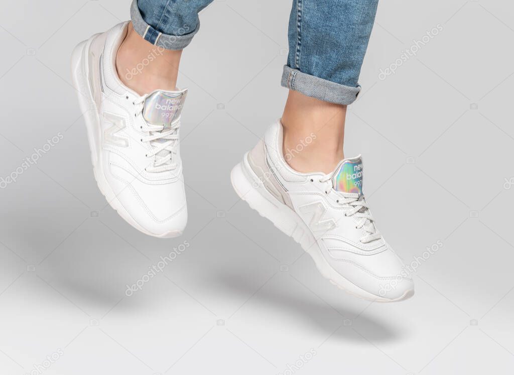 Kiev, Ukraine - January 03, 2021: White women's casual sneakers from New Balance brand on a light background. Young girl in jeans and sneakers on a gray background.