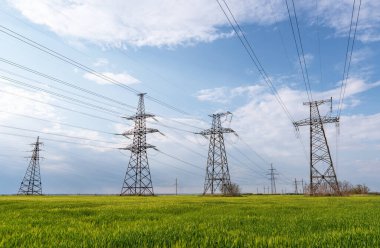 Mavi gökyüzü ve yeşil çayırlar üzerindeki elektrik direkleri..