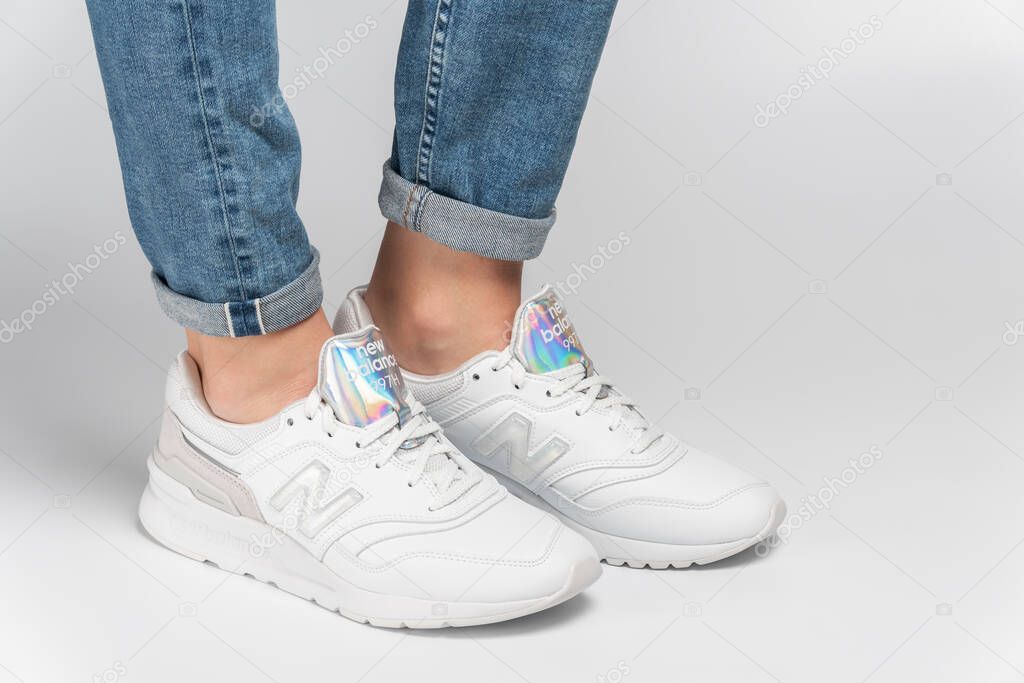 Kiev, Ukraine - January 03, 2021: White women's casual sneakers from New Balance brand on a light background. Young girl in jeans and sneakers on a gray background.